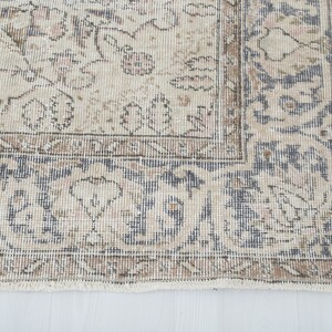 May include: A vintage rug with a beige background and a blue and brown floral pattern. The rug has a fringe border.