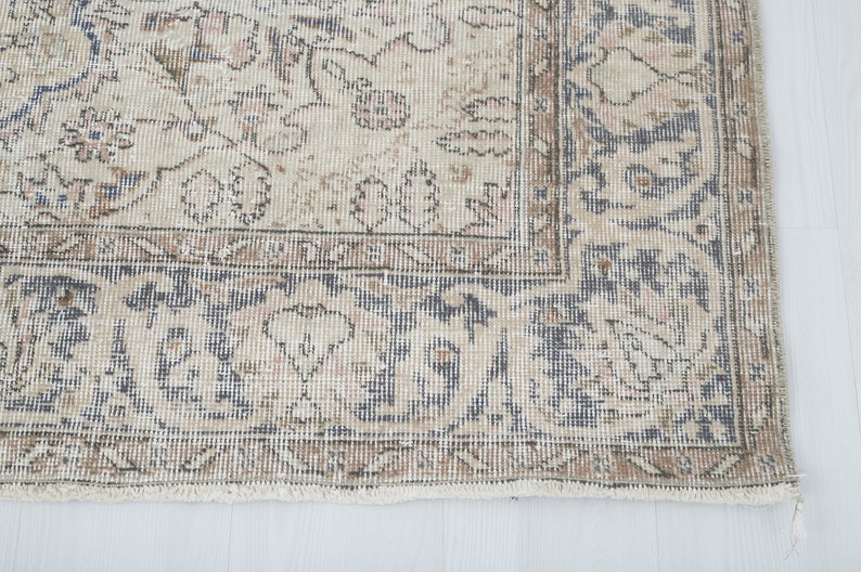 May include: A vintage rug with a beige background and a blue and brown floral pattern. The rug has a fringe border.