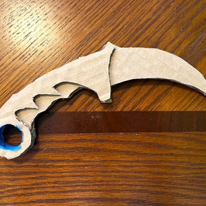May include: A cardboard model of a karambit knife with a blue tape handle.