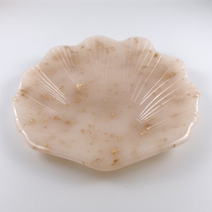 Peut inclure: Un plat en forme de coquille de couleur blanche avec des paillettes dorées. Le plat est en résine et a un bord festonné.