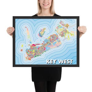 May include: A framed map of Key West, Florida, with a colorful, abstract design. The map features a light blue background with concentric blue lines. The landmass is filled with various colors and patterns, and the words "KEY WEST" are displayed in white.