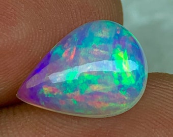 Könnte beinhalten: Ein tropfenförmiger Opal-Edelstein mit einem schillernden Regenbogen-Schimmer, der violette, grüne und rosafarbene Farbtöne zeigt.