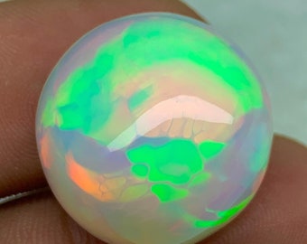 May include: A round, white opal gemstone with green and orange iridescent flashes. The opal is smooth and polished.