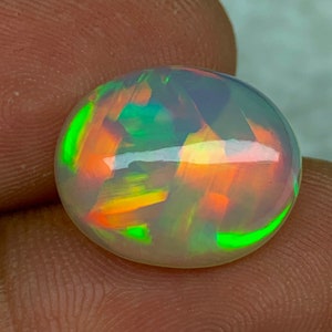 May include: A white opal gemstone with green, orange, and red iridescent flashes. The oval-shaped stone is approximately 10mm in diameter.