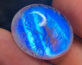 Puede incluir: Una gema redonda, de forma ovalada, iridiscente con un esquema de color azul y blanco. La gema es translúcida y tiene una superficie lisa y pulida.
