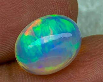 Può includere: Una pietra preziosa di opale ovale bianca con riflessi iridescenti verdi, blu e arancioni.