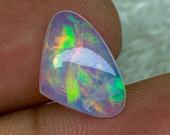 Könnte beinhalten: Ein perlmuttartiger weißer Opal-Cabochon mit irisierenden grünen, blauen und rosa Schimmern. Der Opal hat eine Tropfenform und eine glatte, polierte Oberfläche.