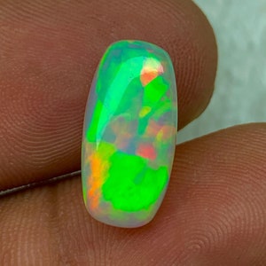 Könnte beinhalten: Ein grüner, weißer und orangefarbener Opal-Cabochon mit einer glatten, polierten Oberfläche. Der Opal ist oval geformt und hat einen lebendigen, irisierenden Glanz.