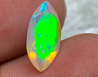 Könnte beinhalten: Ein Opal-Edelstein im Marquise-Schliff mit lebendigen Farben. Der Edelstein zeigt einen leuchtend grünen Kern, umgeben von Blitzen in Blau, Orange und Gelb. Der Stein wird zwischen zwei Fingern gehalten, was seine polierten Facetten zeigt.