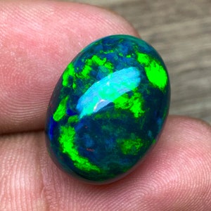 Puede incluir: Una piedra preciosa de ópalo ovalada de color verde oscuro y negro con destellos de verde brillante y azul.