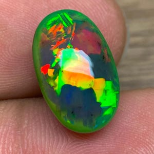 Könnte beinhalten: Ein grüner, schwarzer und regenbogenfarbener Opal-Edelstein mit einer glatten, ovalen Form.