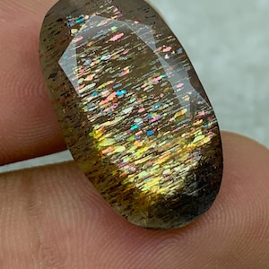 Op de afbeelding: Een grote, ovale edelsteen met een bruine, iriserende en glinsterende uitstraling. De edelsteen heeft een facetgeslepen vorm en toont een regenboog aan kleuren.
