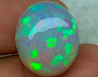 May include: A polished, oval-shaped opal gemstone. The opal displays a play of color with vibrant green and blue hues, set against a milky white base. The stone's surface has a unique, textured appearance.