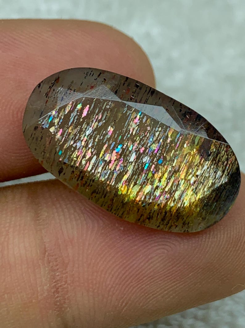 Op de afbeelding: Een grote, ovale edelsteen met een donkerbruine basis en iriserende regenboogkleuren. De edelsteen heeft een glad, gepolijst oppervlak en is gezet in een bezel-setting.