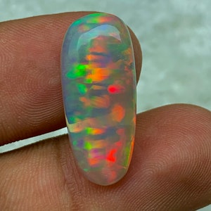 May include: A white opal cabochon with a rainbow of colors, including green, red, orange, and blue.