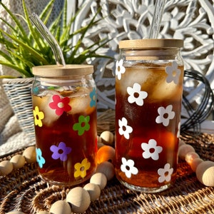 May include: Two glass jars with lids and straws filled with iced tea. The jars are decorated with colorful flower stickers.
