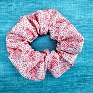 May include: A pink and white fabric scrunchie with a seashell pattern.
