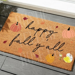 May include: A brown coir doormat with the text "happy fall y'all" in black script. The doormat is decorated with orange and pink pumpkins and brown leaves.