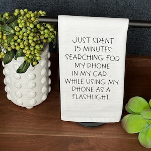 May include: White kitchen towel with black text that reads "Just spent 15 minutes searching for my phone in my car... while using my phone as a flashlight."