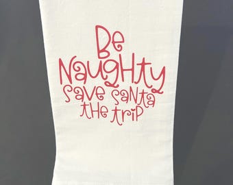 May include: White kitchen towel with red text that reads "Be Naughty Save Santa The Trip".