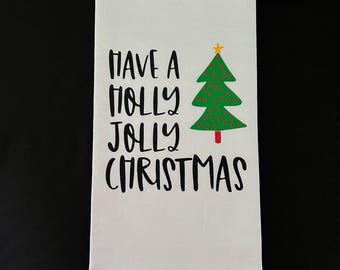 May include: White kitchen towel with black text that reads "Have a Holly Jolly Christmas" and a green Christmas tree with red ornaments and a yellow star on top.