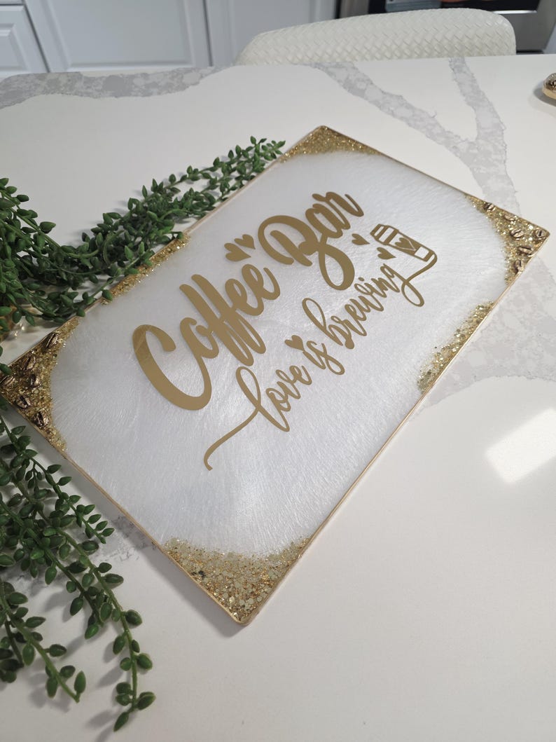 May include: A rectangular white serving tray with gold glitter trim and gold lettering that reads "Coffee Bar Love is brewing". The tray has a white and gold marbled design.