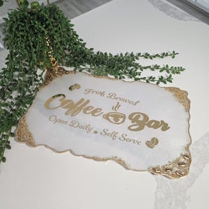 May include: White and gold coffee bar sign with the text "Fresh Brewed Coffee Bar Open Daily Self Serve". The sign has a gold glitter edge and a coffee bean graphic.