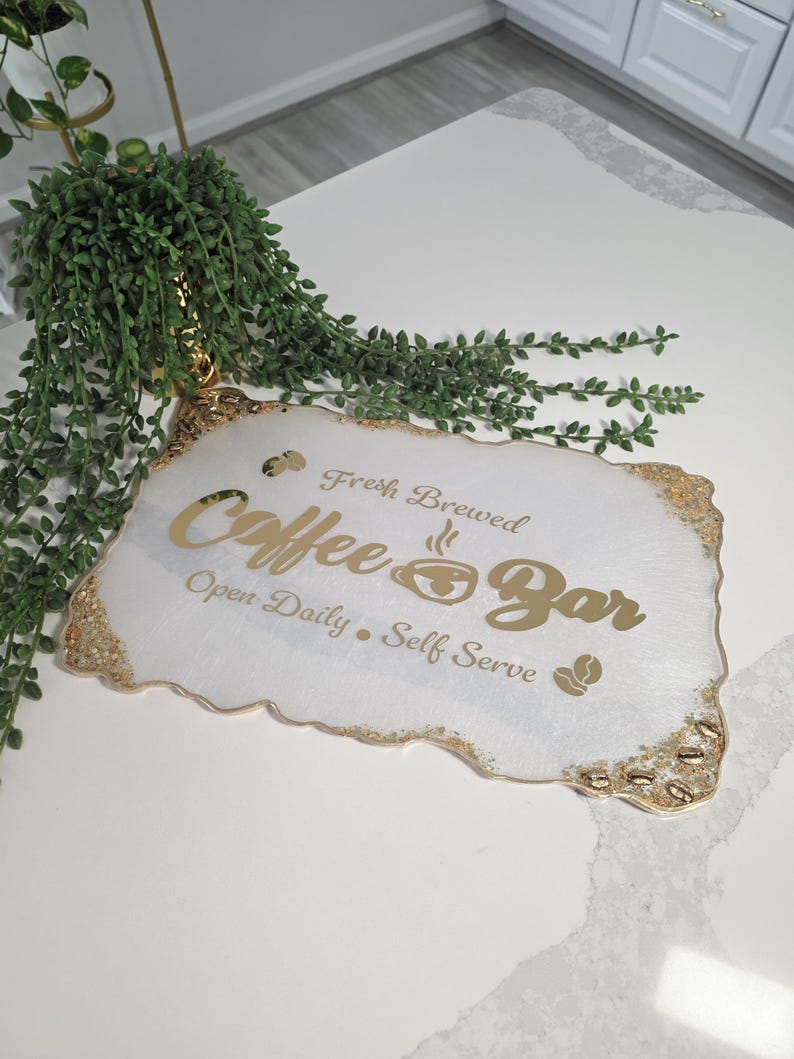 May include: White and gold coffee bar sign with the text "Fresh Brewed Coffee Bar Open Daily Self Serve". The sign has a gold glitter edge and a coffee bean graphic.