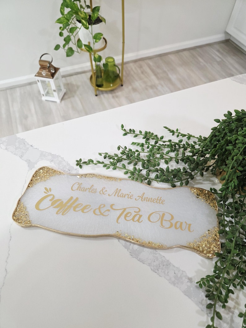 May include: A white resin sign with gold glitter edging, featuring the text "Charles & Marie Annette Coffee & Tea Bar" in gold script. The sign is rectangular with organic edges, suitable for a home coffee station.