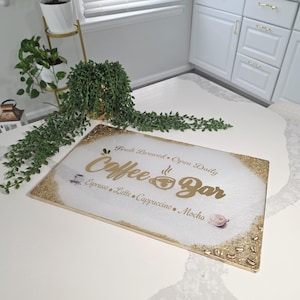 May include: A rectangular "Coffee Bar" sign with gold lettering and a gold glitter border. The sign lists coffee drinks like espresso, latte, and cappuccino. The background is white with a subtle marble effect.