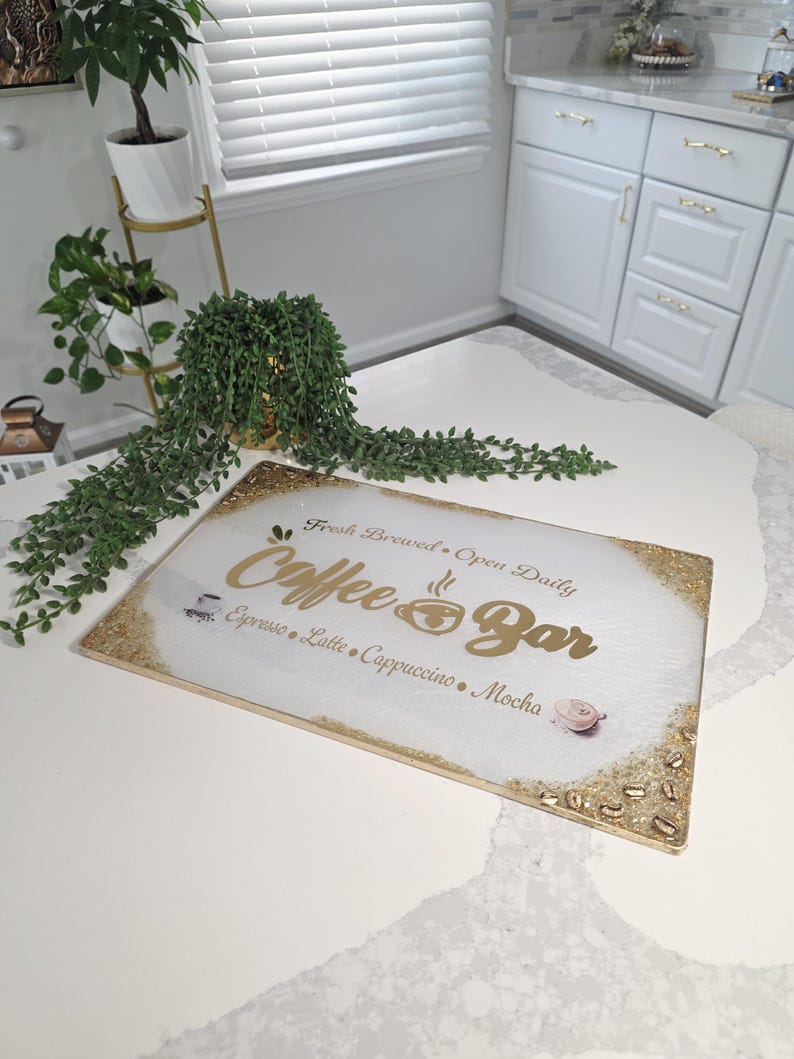 May include: A rectangular "Coffee Bar" sign with gold lettering and a gold glitter border. The sign lists coffee drinks like espresso, latte, and cappuccino. The background is white with a subtle marble effect.