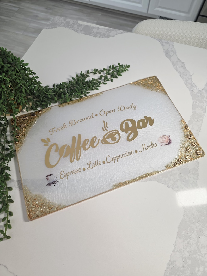 May include: A rectangular coffee bar sign with a white background and gold glitter trim. The sign features the words "Coffee Bar" in gold script, along with coffee-related terms and phrases.