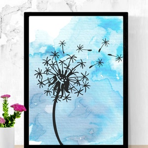 May include: Black framed art print featuring a silhouette of a dandelion with seeds blowing away against a watercolor blue background. The artwork is displayed on a wooden surface with a white vase of pink flowers.