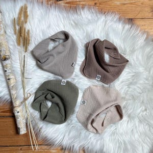Könnte beinhalten: Vier verschiedene farbige Mull-Babyspucktücher. Die Spucktücher sind in Braun-, Beige- und Grüntönen gehalten. Die Spucktücher sind aus einem weichen, saugfähigen Material gefertigt und perfekt, um die Kleidung des Babys sauber zu halten.