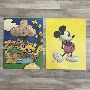 Könnte beinhalten: Zwei Vintage-Kunstwerke zum Thema Disney. Eines zeigt eine Patchwork-Landschaft mit Mickey und Minnie Mouse. Das andere ist ein gelber Druck von Mickey Mouse in einer Gehpose. Beide werden auf einer Holzoberfläche ausgestellt.