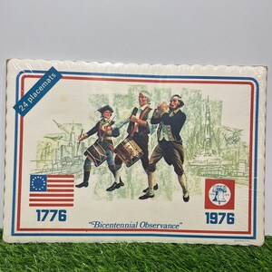 May include: A set of 24 placemats featuring a vintage illustration of three men in colonial attire marching with drums. The placemats are decorated with the American flag, the Liberty Bell, and the years 1776 and 1976. The text "Bicentennial Observance" is printed below the illustration.