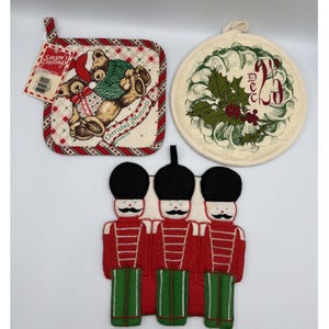 May include: Three fabric pot holders: one square with a teddy bear and 'Season's Greetings' tag, one round with a holly wreath and 'DEC 25' text, and one shaped like three toy soldiers in red uniforms with black hats and green trousers.