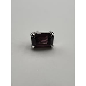 May include: A silver-toned stud earring featuring a rectangular, deep purple gemstone. The gemstone is set within a four-prong setting, showcasing its rich color and geometric shape. The earring is designed for a classic and elegant look.