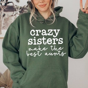 May include: A green hooded sweatshirt with the text "crazy sisters make the best aunts" printed in white.