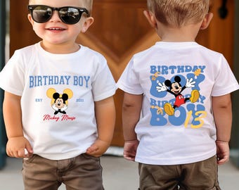 May include: Two white t-shirts with a blue and yellow Mickey Mouse design. The front of one shirt says "Birthday Boy Est 2013 Mickey Mouse" and the back of the other shirt says "Birthday Boy" with a Mickey Mouse graphic.