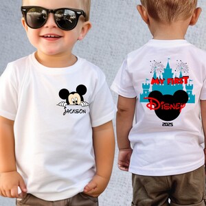 May include: White t-shirts with a Mickey Mouse design. One shirt has "Jackson" printed below the character. The other shirt has "My First Disney" and "2025" printed on the back, with a Mickey Mouse silhouette and castle graphic.