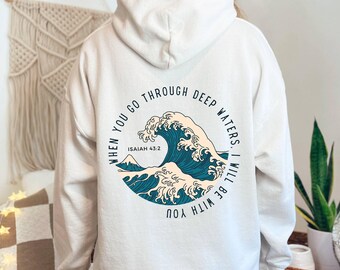 May include: Cream-colored hoodie with a teal and white wave graphic. The graphic includes the text "WHEN YOU GO THROUGH DEEP WATERS, I WILL BE WITH YOU" and "ISAIAH 43:2" in a circular design. The hoodie has a hood and long sleeves.