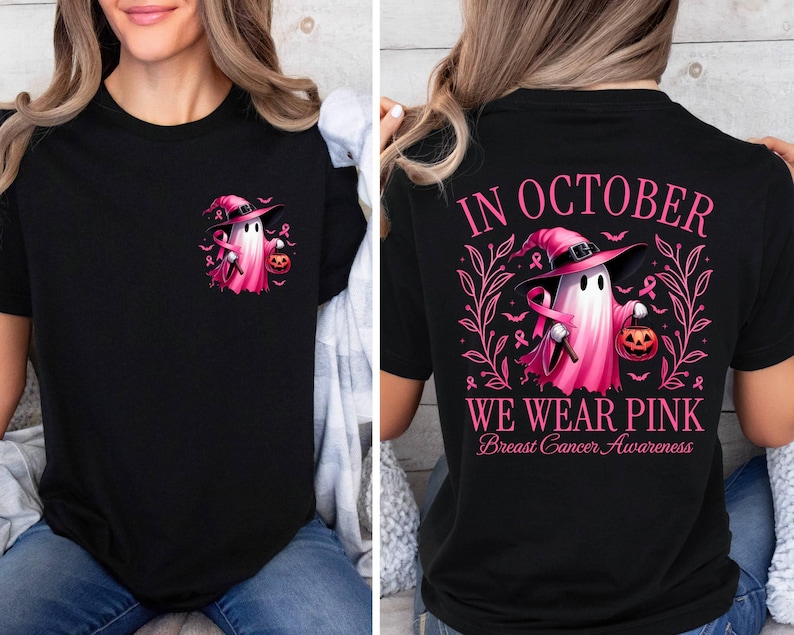 May include: Black t-shirt featuring a pink ghost wearing a witch's hat and holding a pumpkin. The text "In October We Wear Pink Breast Cancer Awareness" is printed on the shirt.