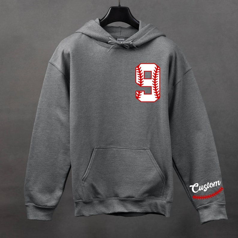 K&ouml;nnte beinhalten: Grauer Kapuzenpullover mit einer wei&szlig;en Baseball-Nummer 9 auf der Vorderseite und roten N&auml;hten. Das Wort "Custom" befindet sich auf dem &Auml;rmel mit roten N&auml;hten.