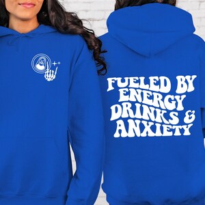 Puede incluir: Una sudadera con capucha azul real con texto blanco que dice "Fueled by Energy Drinks & Anxiety". La parte delantera de la sudadera tiene un gr&aacute;fico blanco de una mano de esqueleto sosteniendo una lata con una pesta&ntilde;a de apertura.