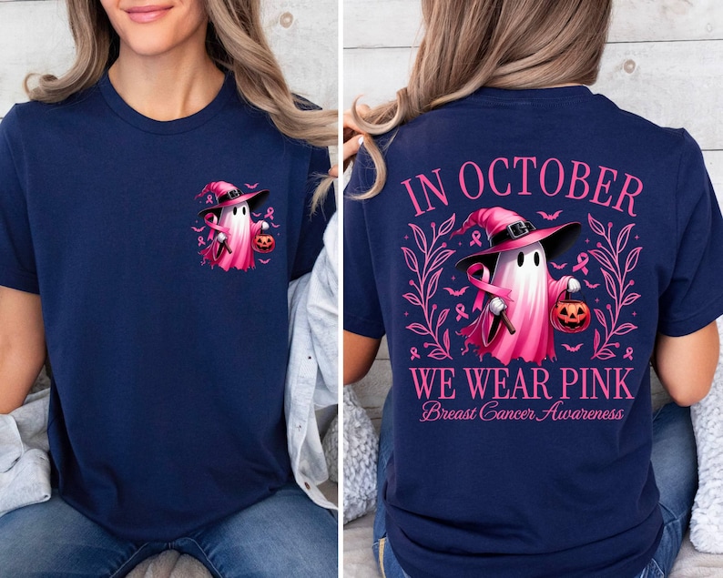 May include: A navy blue t-shirt featuring a pink ghost wearing a witch's hat and holding a pumpkin. The back of the shirt reads "In October We Wear Pink Breast Cancer Awareness".