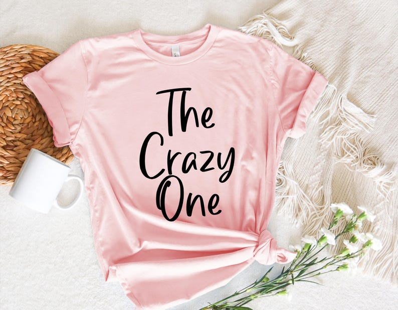 Peut inclure: Un t-shirt rose avec le texte "The Crazy One" imprim&eacute; en noir.