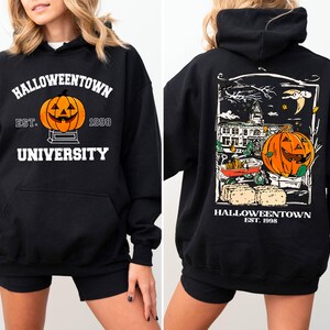 May include: Black hooded sweatshirt with a Halloween theme. The front features a jack-o'-lantern and the text "Halloweentown University Est. 1998." The back displays a detailed graphic of a pumpkin, buildings, and the text "Halloweentown Est. 1998."