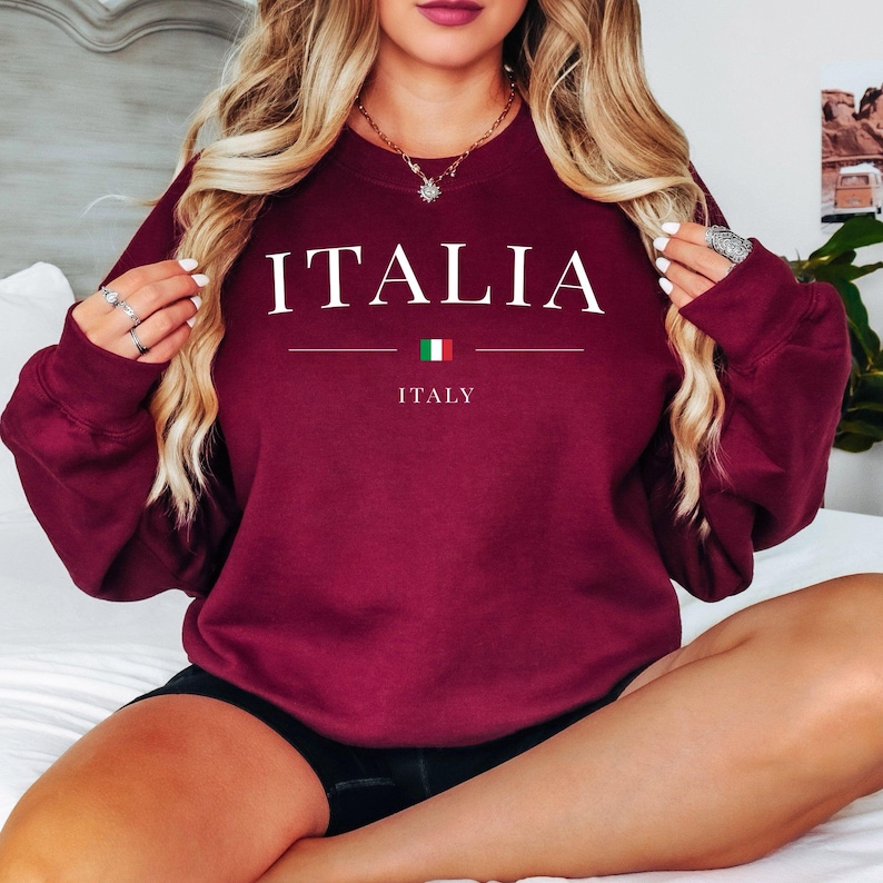 May include: Burgundy crewneck sweatshirt with the word "ITALIA" in white block letters. Below the word is a horizontal line, the Italian flag, and the word "ITALY". The sweatshirt is a solid color.