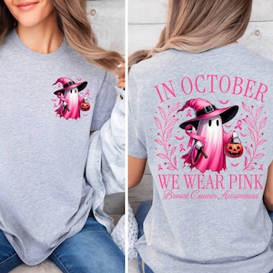 May include: Grey t-shirt with a pink ghost wearing a witch hat and holding a pumpkin. The text on the back of the shirt reads "In October We Wear Pink Breast Cancer Awareness."